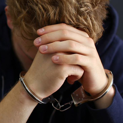 Man wearing handcuffs sitting in a jail cell, appearing vulnerable