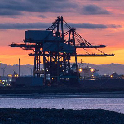 Industrial facilities and shipping containers at a busy port, with cranes and infrastructure in view