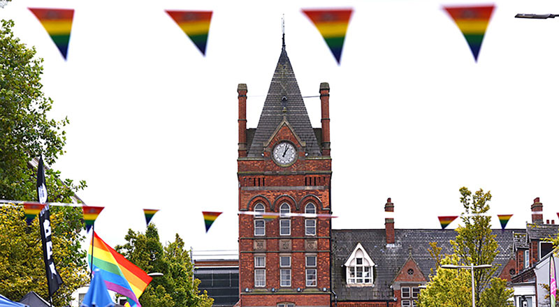 The Waterhouse Building clock tower at Teesside University, with pride flags in the foreground. Link to Pride 2025 LGBTQ+ books in the Library.