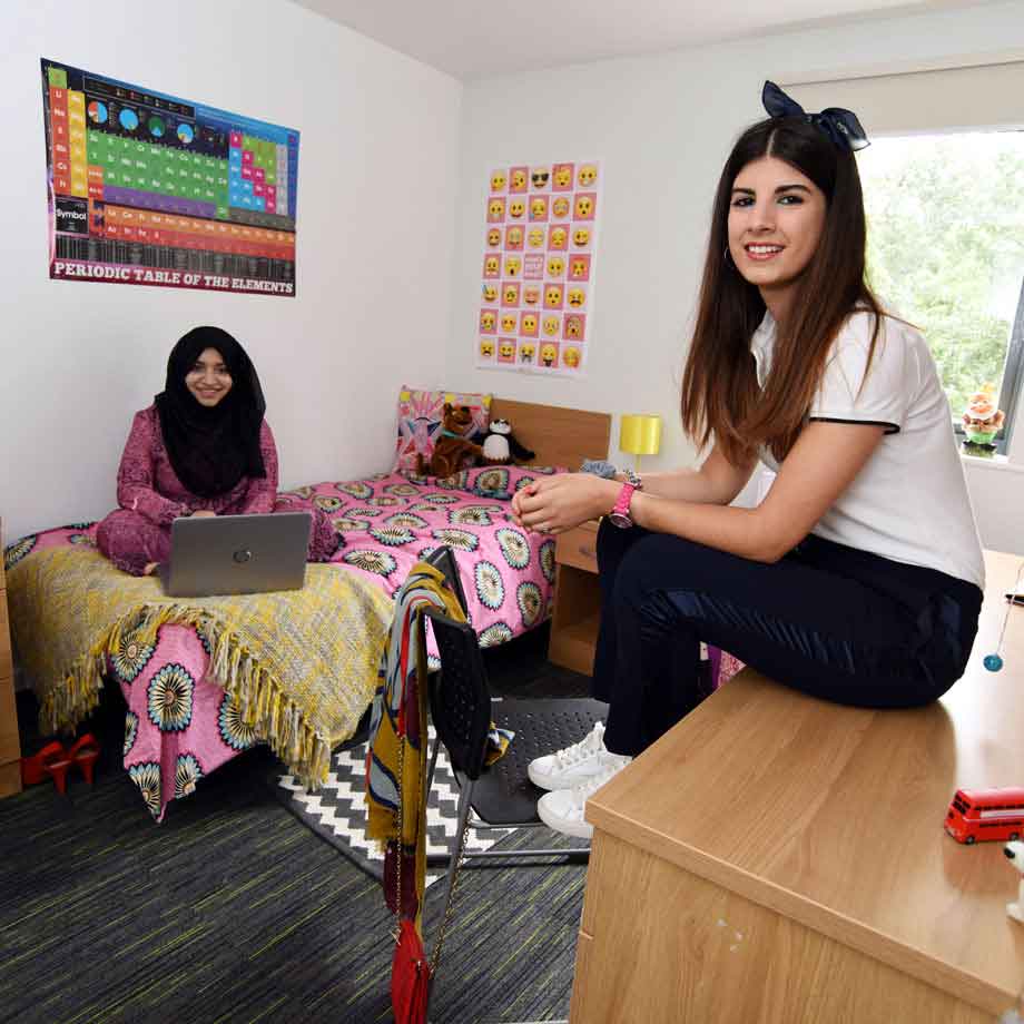 One student lying on the bed and another sitting at the desk in a shared bedroom at West Parkside Village student accommodation