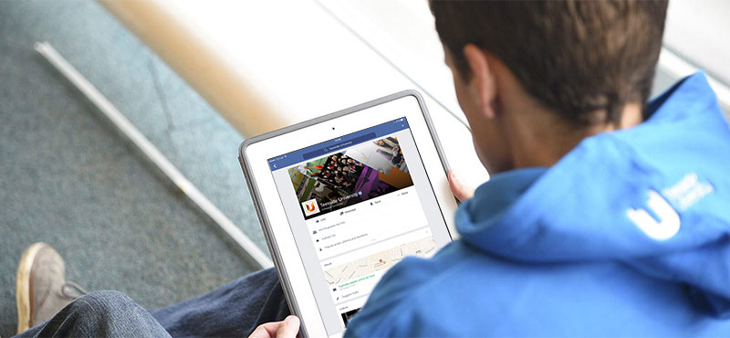 Student sitting at a table viewing Teesside University Facebook page on a device