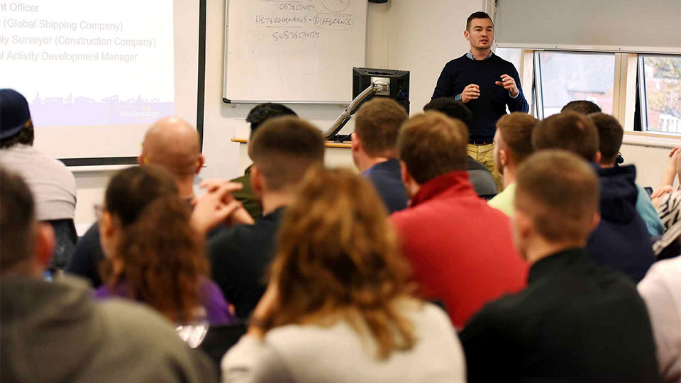Speaker presenting at a conference event with attendees listening at Teesside University