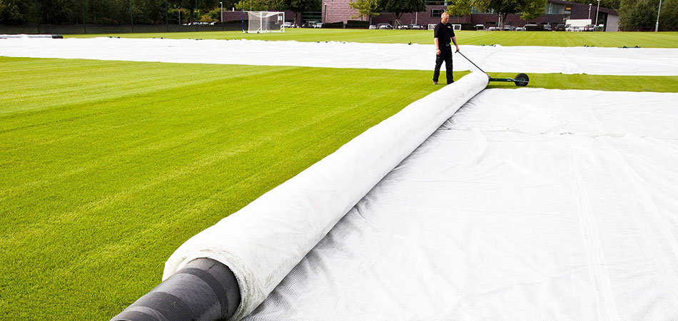 Man extending Machsaver pitch covers on a sports field