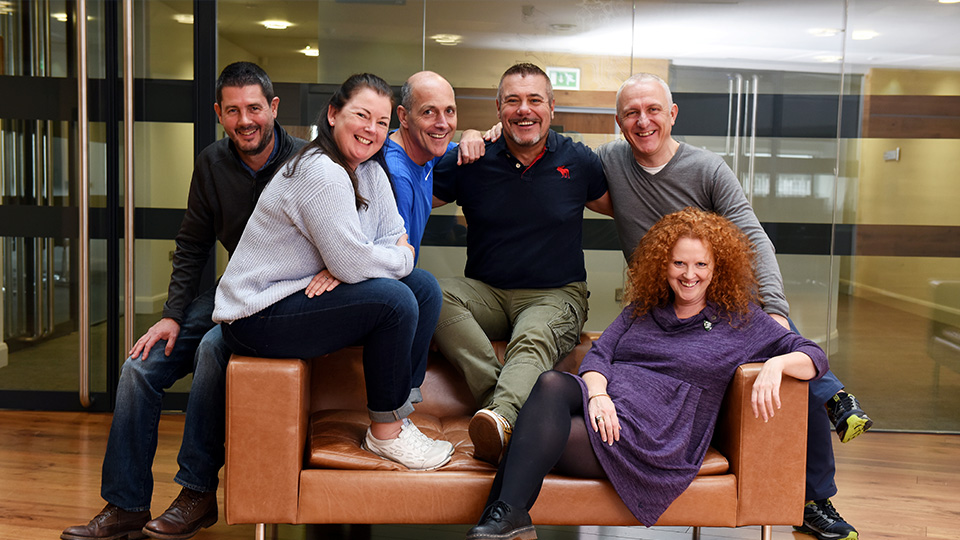 Teesside University alumni gathered and posing together on a sofa at a reunion event.