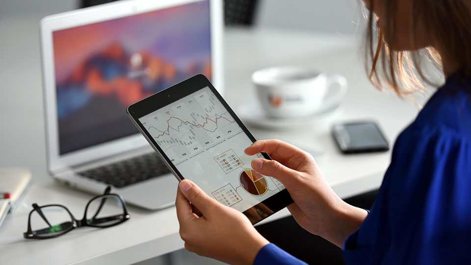 Woman holding a tablet showing financial graphs and data visualizations
